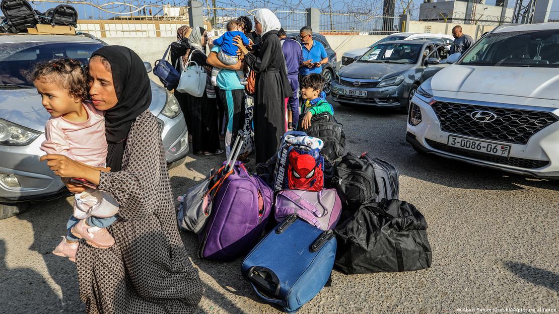 Women laden down with luggage and young children surrounded by cars