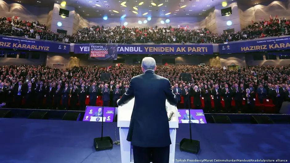 Turkish President Recep Tayyip Erdogan seen from behind standing at a podium on stage before a full auditorium