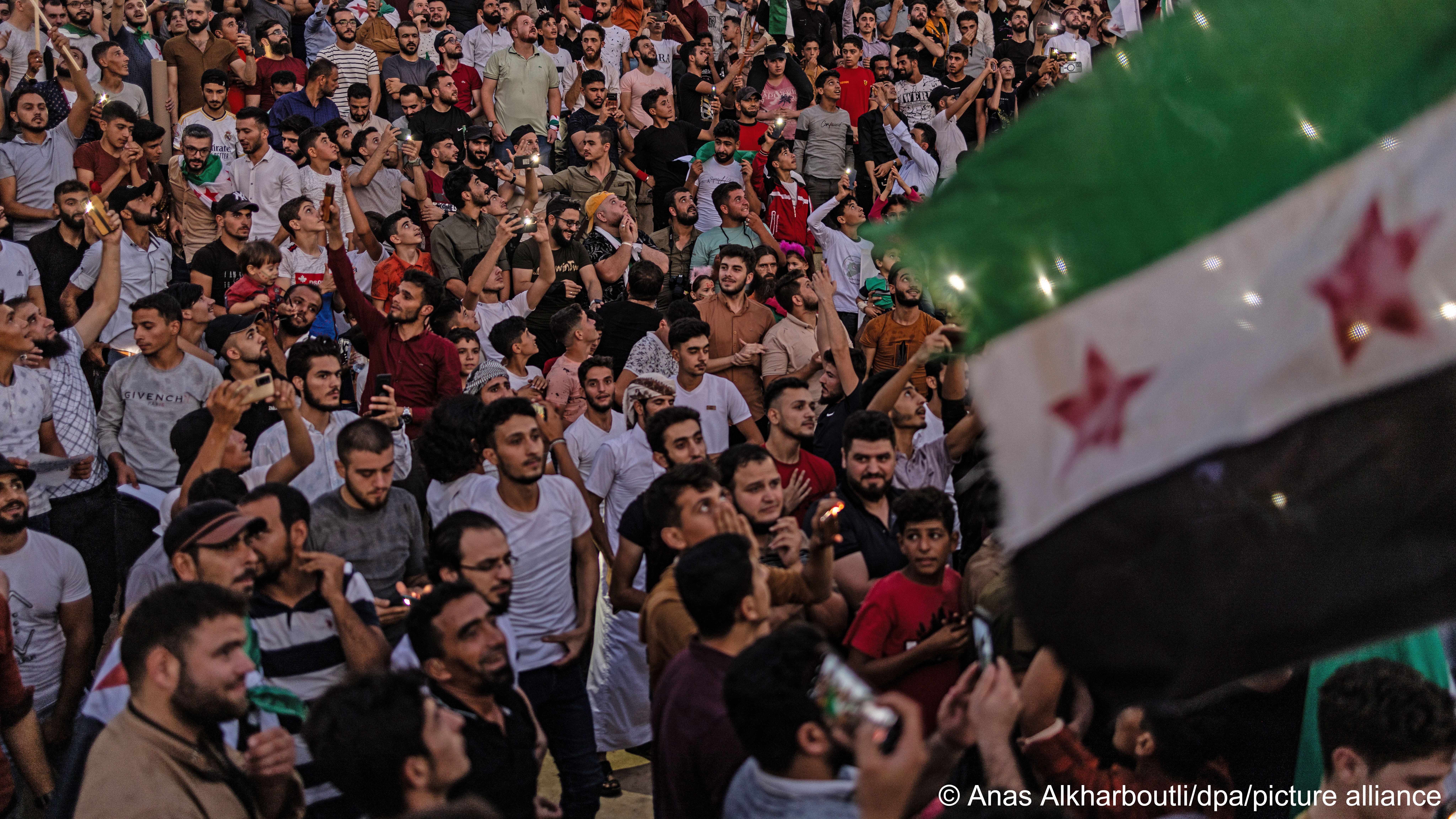 A crowd of protesters can be seen behind a Syrian flag, Idlib, Syria, 25 August 2023