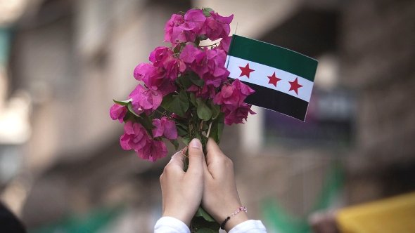 In this Friday, Sept. 21, 2012 photo, a Syrian woman holds a bouquet of flowers and rebel flag during a demonstration in the Bustan al-Qasr neighborhood of Aleppo, Syria. (photo: Manu Brabo/AP/dapd)