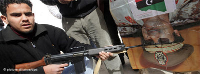 Libyer hält eine Waffe an ein Gaddafi-Poster; Foto: dpa