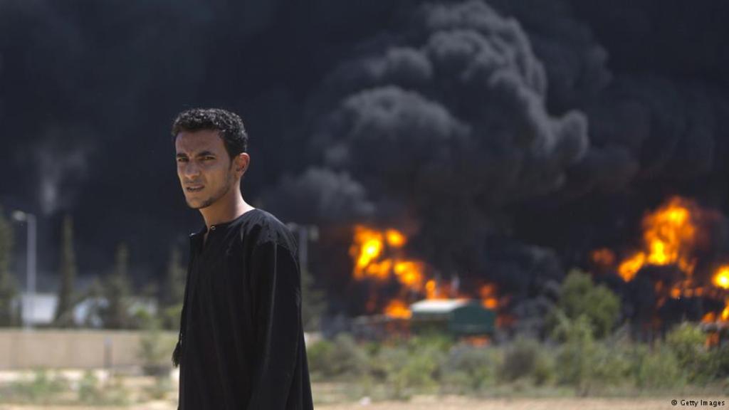 A Palestinian man in front of a burning power plant in Gaza after it was hit by Israeli shelling on 29 July 2014 (photo: Getty Images)