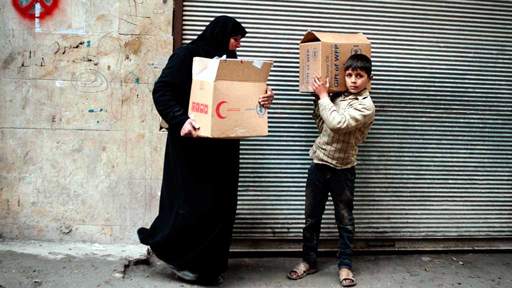 eine syrische Frau und ihr Sohn transportieren Kartons mit Lebensmitteln in der nordsyrischen Stadt Aleppo.