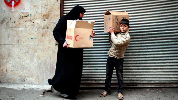 A Syrian woman and her son transporting boxes with food in Aleppo (photo: dpa/picture-alliance)