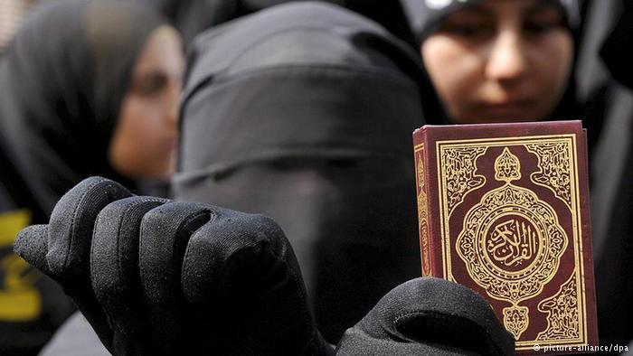 A woman wearing a niqab and holding up a Koran (photo: dpa/picture-alliance)