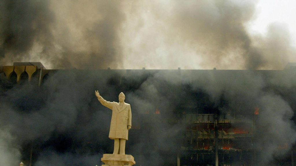 تمثال صدام أمام مبنى يحترق في بغداد عام 2013. Foto: AFP/picture-alliance 