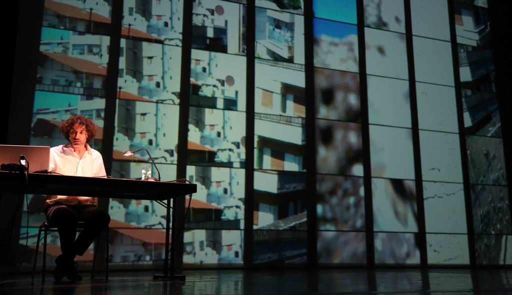 Mroué sitzt vor einer Projektionswand während The Pixelated Revolution;source:kampnagel.de