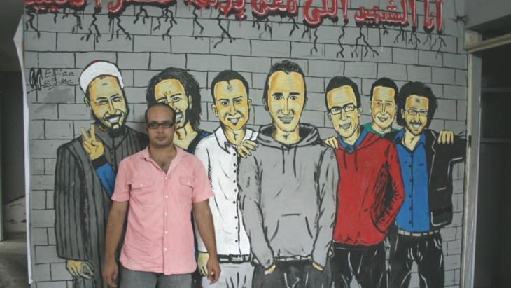 Ahmed Maher vor einem Revolutionsgrafitti in Kairo; Foto: Markus Symank