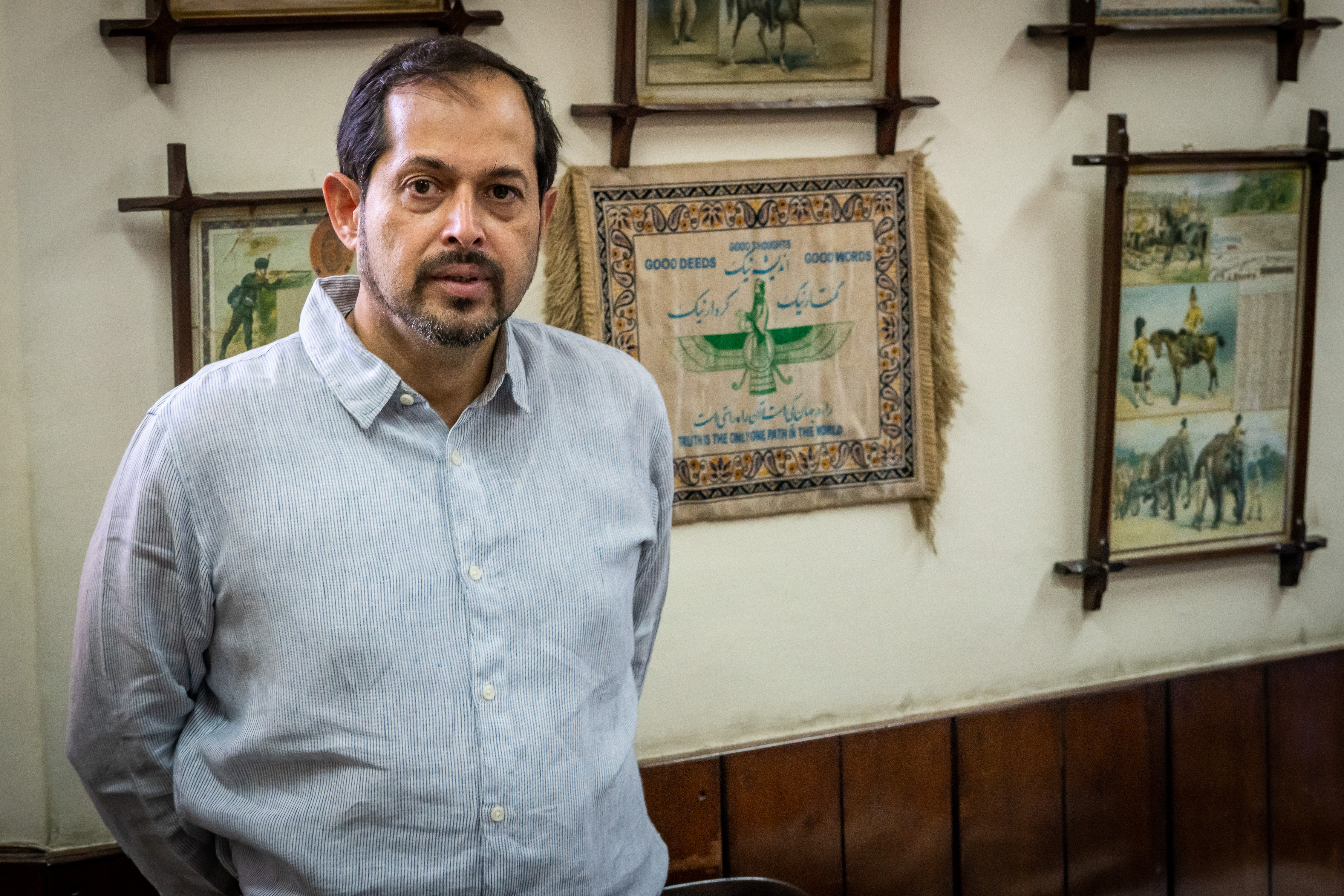 Isphanyar Bhandara poses in his office for a photo. Behind him is a wall-hanging displaying the main tenets of the Parsi faith: "Good thoughts, good deeds, good words" (photo: Philipp Breu)