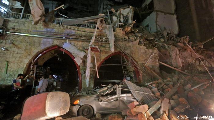 People stand by a building and car in ruins in the evening in Beirut (photo: Getty Images/AFP/STR)