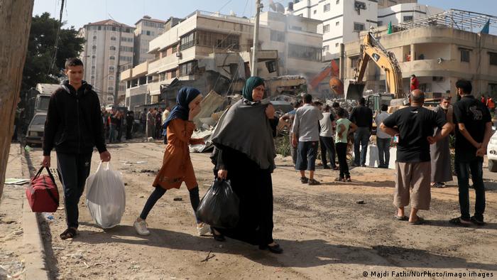 People move about Gaza with bags of belongings as crowds watch tractors clearing rubble