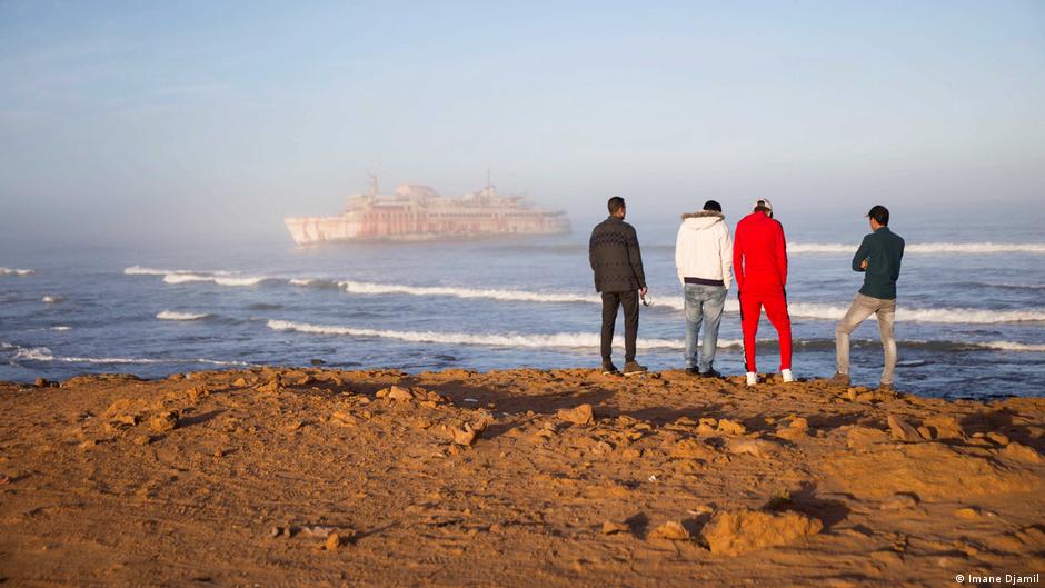 Hassan Boulahcen, 27, a surf coach, Maatoug, Hossin Ofan, 34, Nuevas Olas surf club general coordinator, and Oussama Segari, 26, who works as the club's treasurer and coffee shop manager, face the sea in front of the Armas shipwreck (photo: Imane Djamil)
