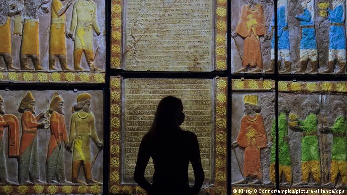 Eine Museumsbeobachterin steht vor einer Farbprojektion, die Reliefs darsteltt.