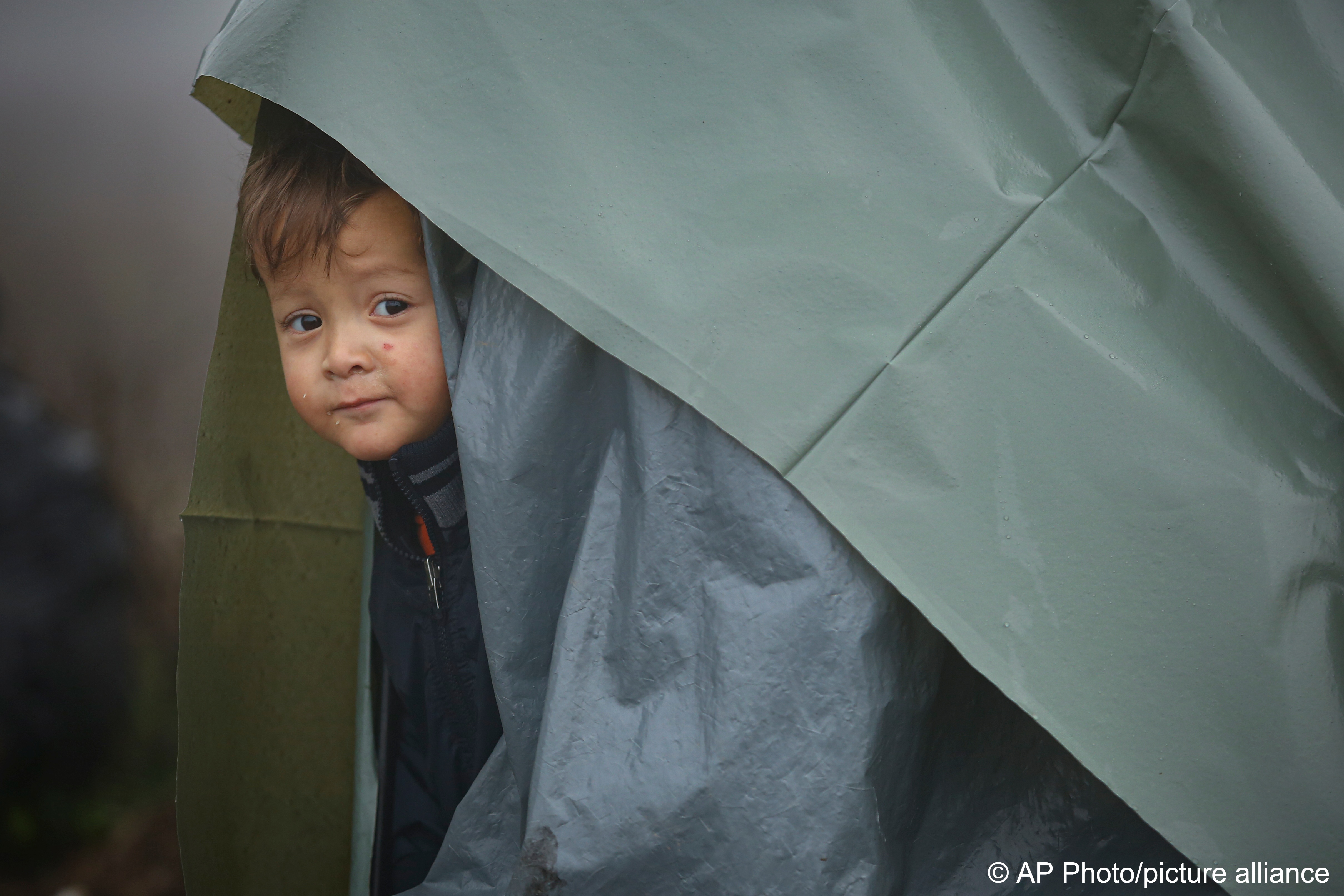 Ein Migrantenkind blickt aus einem behelfsmäßigen Zelt in einem Lager für Migranten, die hauptsächlich aus Afghanistan stammen, in Velika Kladusa, Bosnien, am 12. Oktober 2021; Foto: AP Photo