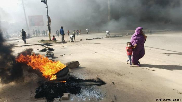 A Sudanese woman and child walk past burning tyres used by protesters in an attempt to block a road in Khartoum, Sudan (photo: AFP/Getty Images)