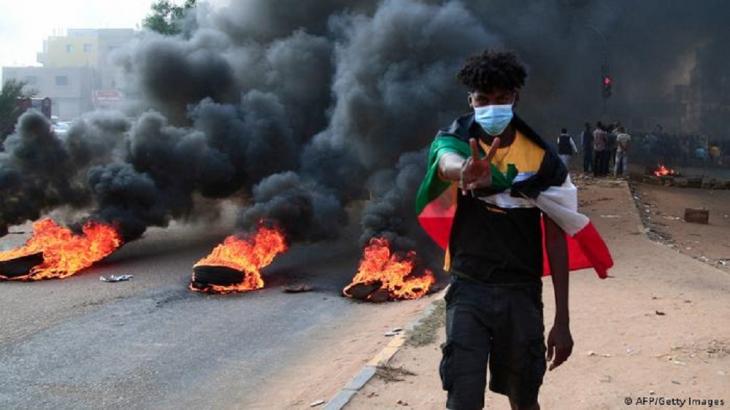 A Sudanese protester draped in the Sudanese flag flashes the victory sign next to burning tyres, Khartoum, Sudan , 25 October 2021 (photo: AFP/Getty Images)