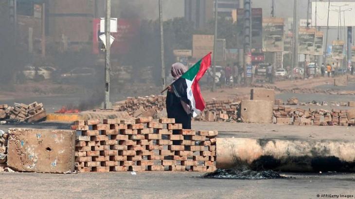 A Sudanese woman holds the Sudanese flag beside a roadblock set up by protesters, Khartoum, Sudan, 26 October 2021 (photo: AFP/Getty Images)