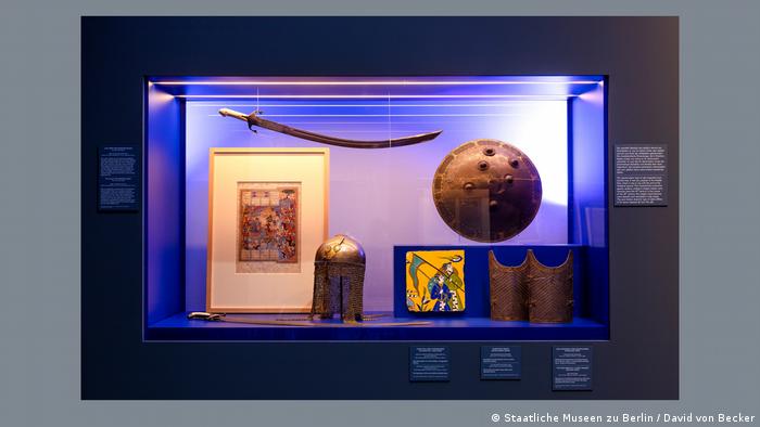 A museum display case featuring an ancient sword, shield, helmet and various paintings