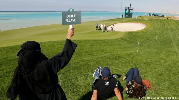 Bei der Saudi Golf Championship hält eine verschleierte Frau am Rande des Golfkurses ein Schild mit der Aufschrift "Quiet please!"