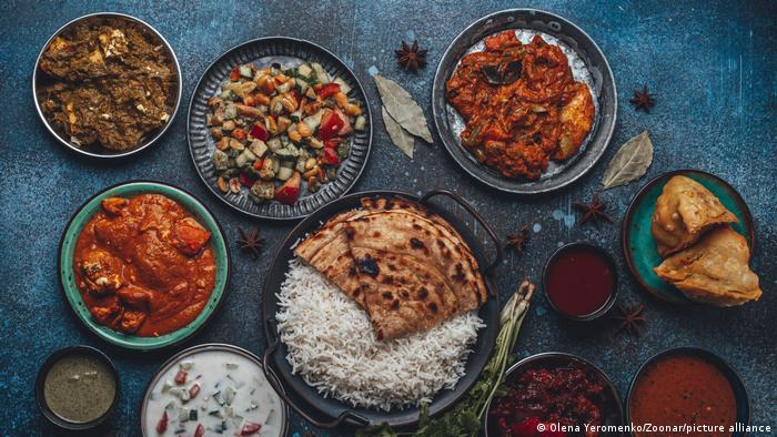 Verschiedene indische Spezialitäten auf einer Platte mit Gewürzen dekoriert. Darunter Reis und Chapati sowie verschiedene Soßen, Curries und Gemüse.