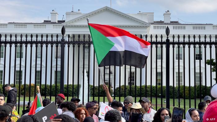 People stand outside the White House fence in Washington, one person waves a Sudanese flag.