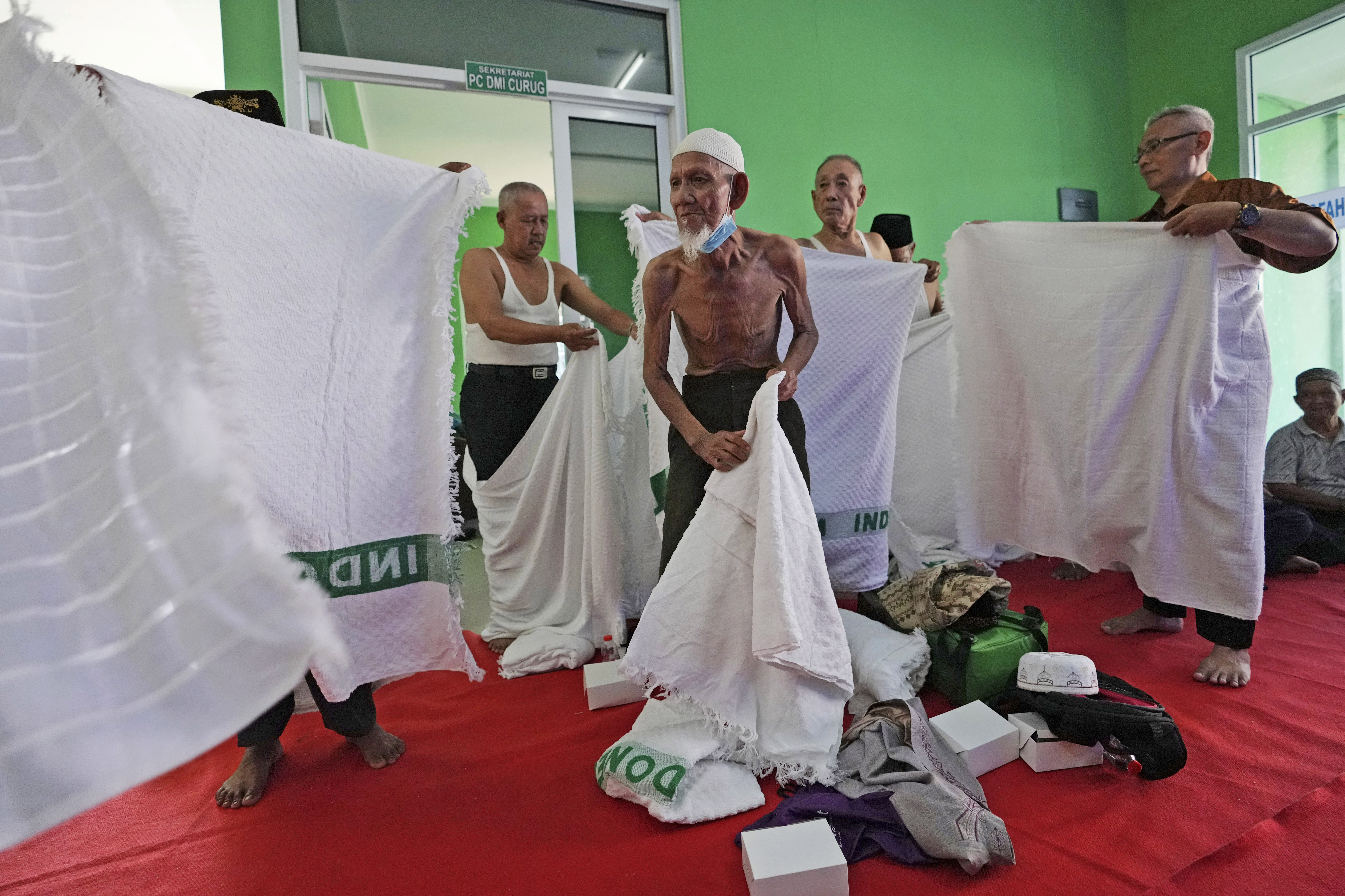 Husin bin Nisan, center, with other worshippers, prepares to wear a special garb called "ihram," typically worn during hajj pilgrimage, prior to a hajj rehearsal in Tangerang, Indonesia, Monday, May 15, 2023. After spending more than three decades picking tips from motorists, the 85-year-old volunteer traffic attendant is finally realizing his dream to go to the Islamic holy cities of Mecca and Medina for hajj pilgrimage (image: AP Photo/Achmad Ibrahim)