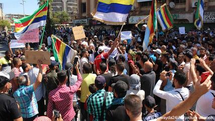 صورة من: Suwayda24/AP/picture alliance التظاهر والجتمع الاحتجاجي مستمر في ساحة الكرامة وسط السويداء. Protesters hold up placards and wave Druze flags, Sweida city, Syria, 27 August 2023