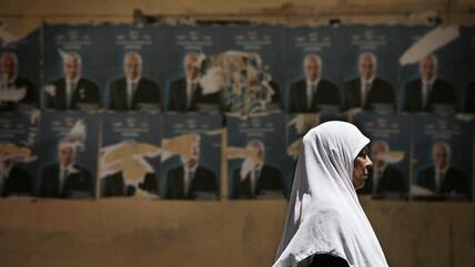 An Egyptian woman walks past election posters for the upcoming elections in Cairo (photo:AP)