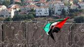 A Palestinian flag is caught in barbed wire near the Israeli West Bank barrier; houses can be seen in the background