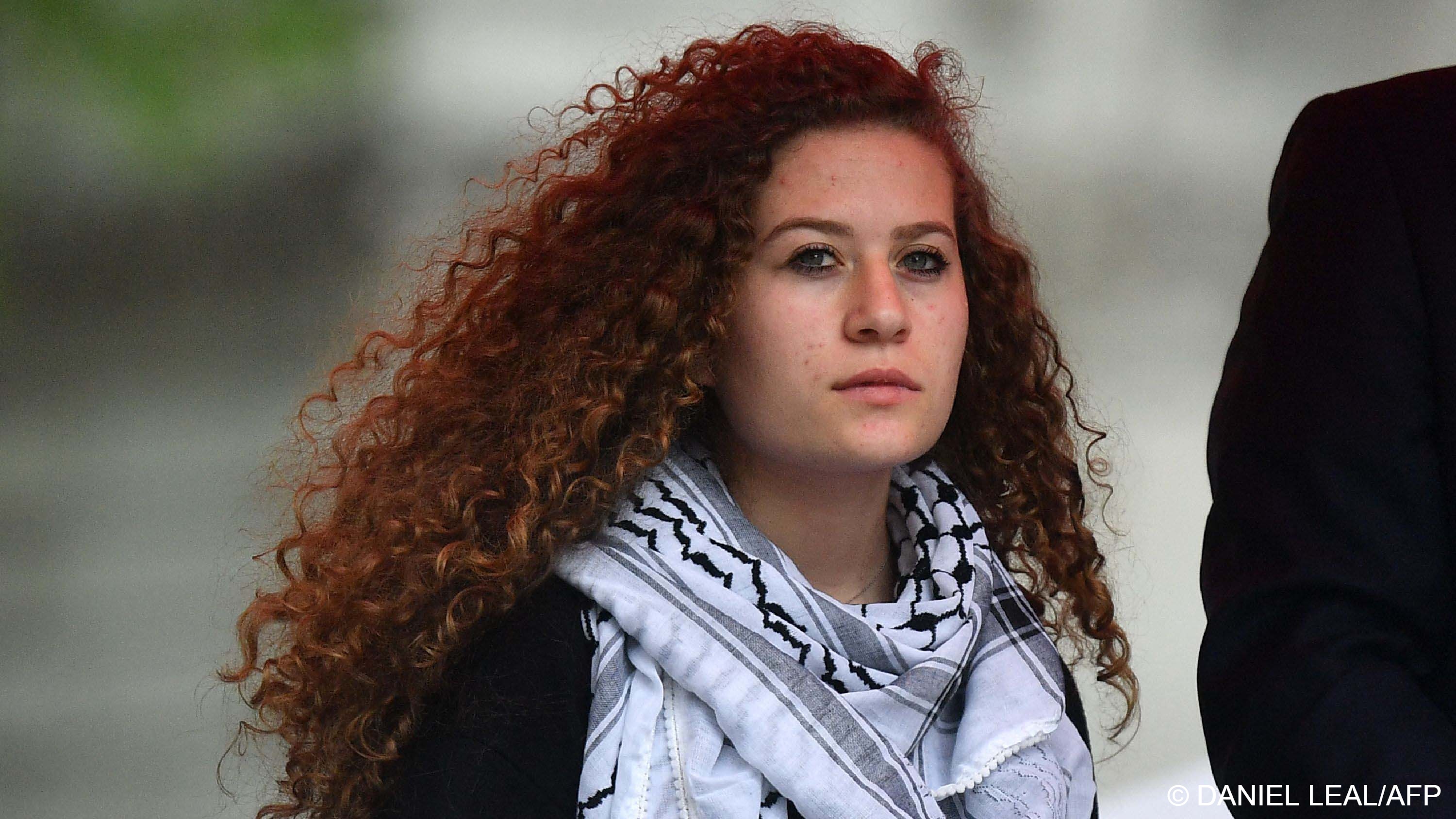 Portrait of a young woman with long curly brown hair wearing a Palestinian keffiyeh scarf