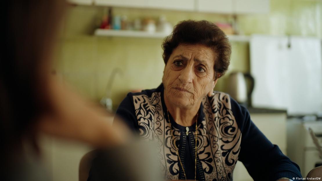 An older woman (Nuha Tarazi) sits at her kitchen table, a pained expression on her face