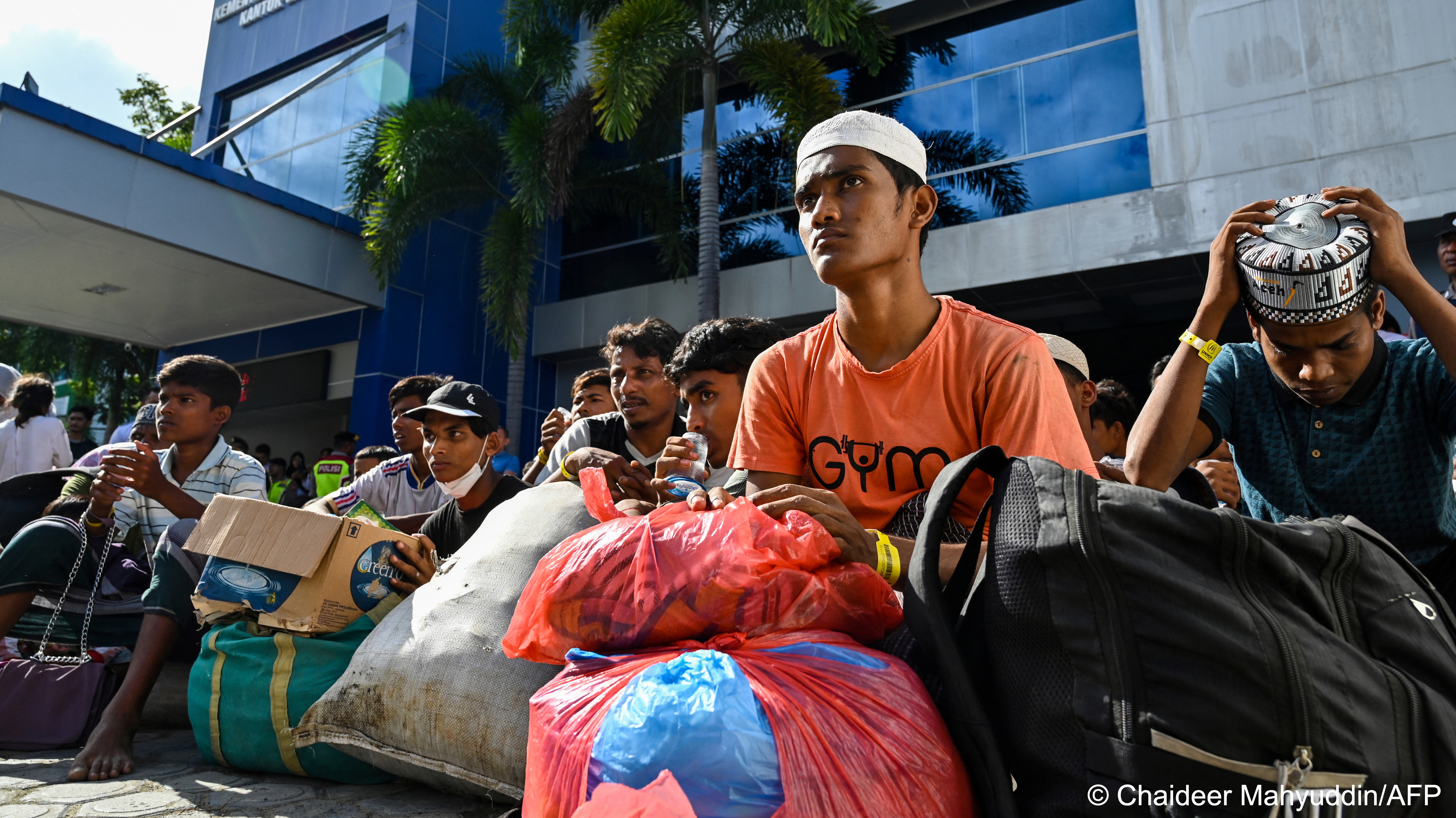 Rohingya refugees sit on the ground with bags of belongings in front of a government building, Banda Aceh, Indonesia, 27 December 2023