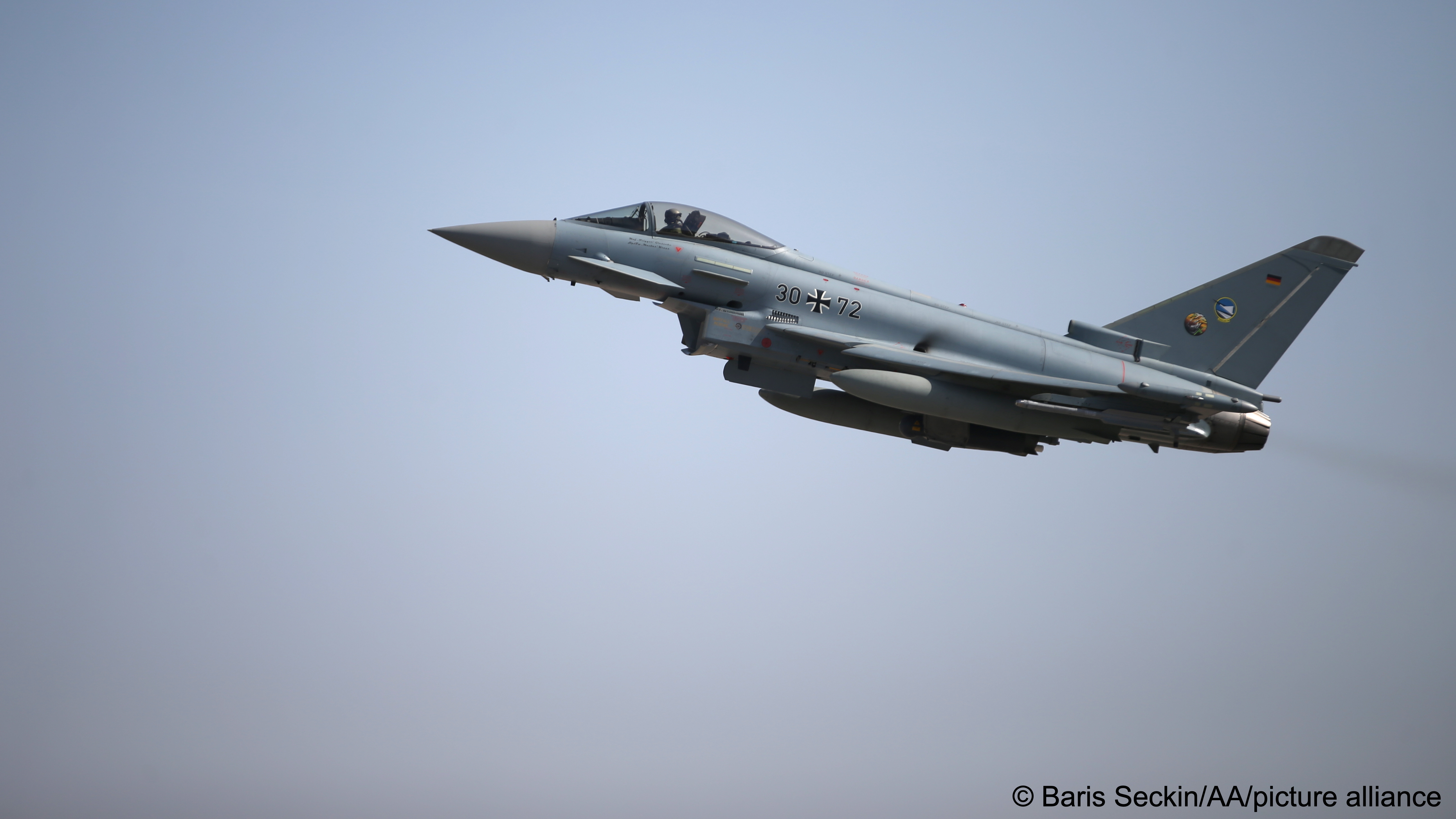 A German Air Force Eurofighter Typhoon fighter jet flies across a grey sky