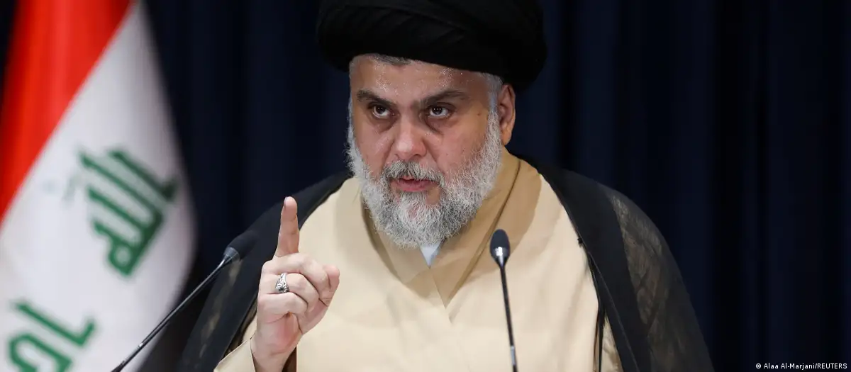 Headshot of Iraqi Shia cleric, politician and populist Muqtada al-Sadr; on his left is an Iraqi flag