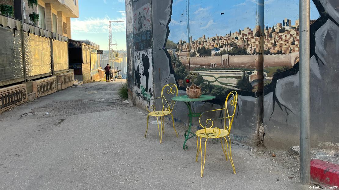 A mural of Jerusalem on Israel's separation barrier, which separates Bethlahem from neighbouring Jerusalem, on an empty street. Next to the wall are a green table and two yellow chairs, both empty