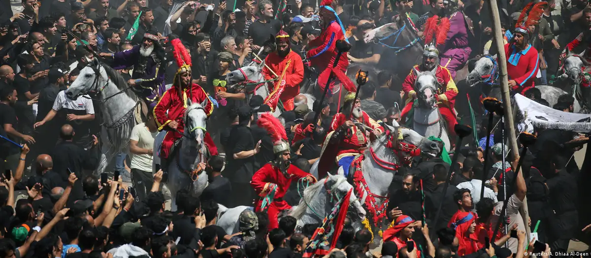 A dense crowd of people gathers around a group of horses ridden by men in colourful historical costumes during the re-enactment of the Battle of Karbala, Iraq