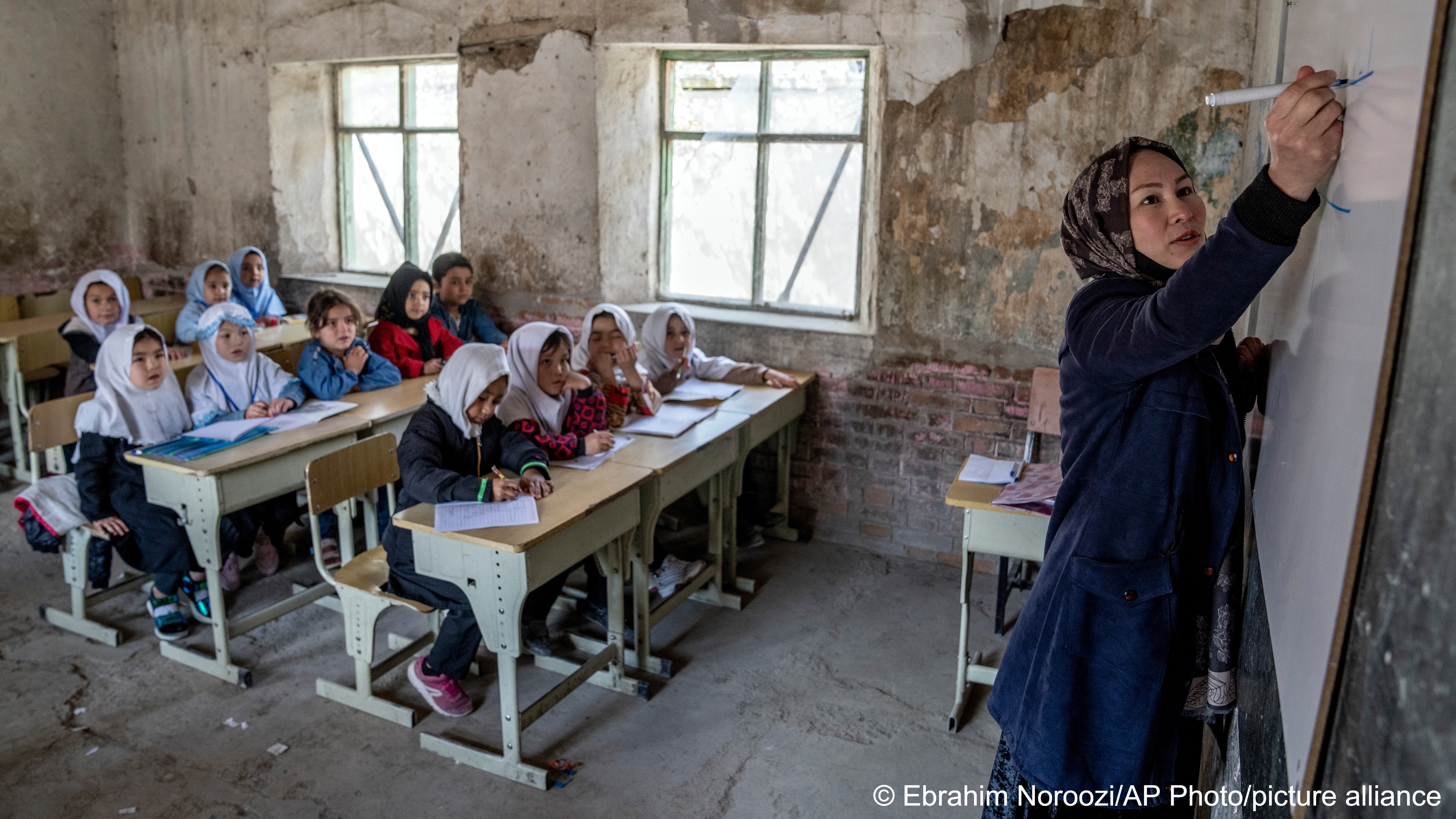 A female teacher writes on a white board while watched by a class of girls in headscarves on the first day of the school year, Kabul, Afghanistan, 25 March 2023