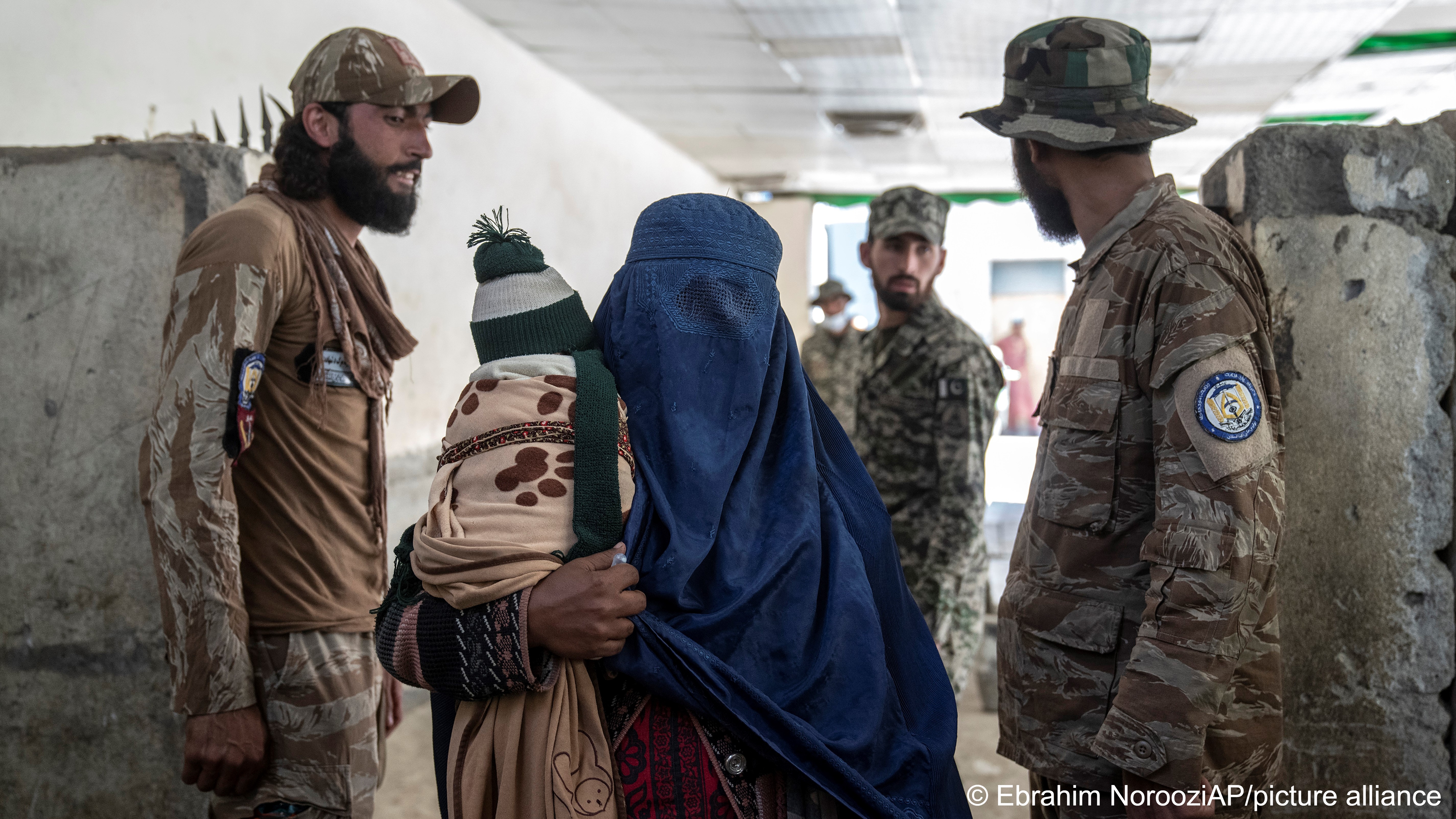 An Afghan refugee woman dressed in a burqa and carrying a child passes two soldiers on her return to Afghanistan through the Pakistan-Afghanistan border in Torkham, Afghanistan, 3 November 2023