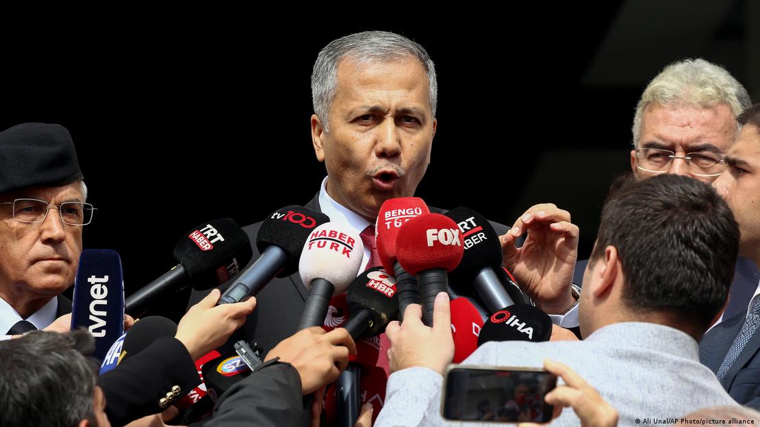 Interior Minister Ali Yerlikaya, who is surrounded by people, gestures with his left hand as he speaks into an array of microphones being held up to his face, Ankara, Turkey, 1 October 2023