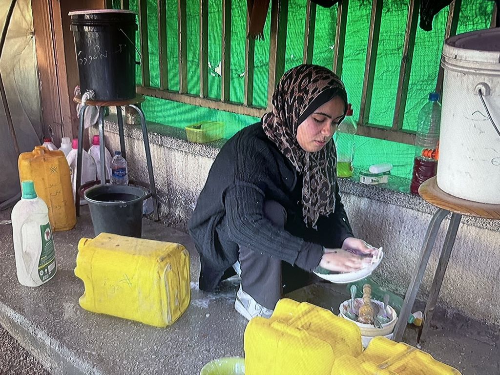 A woman in an animal-print headscarf and black clothes (Menna Hamouda) crouches on the ground as she mixes colours; all around her are plastic bottles and canisters