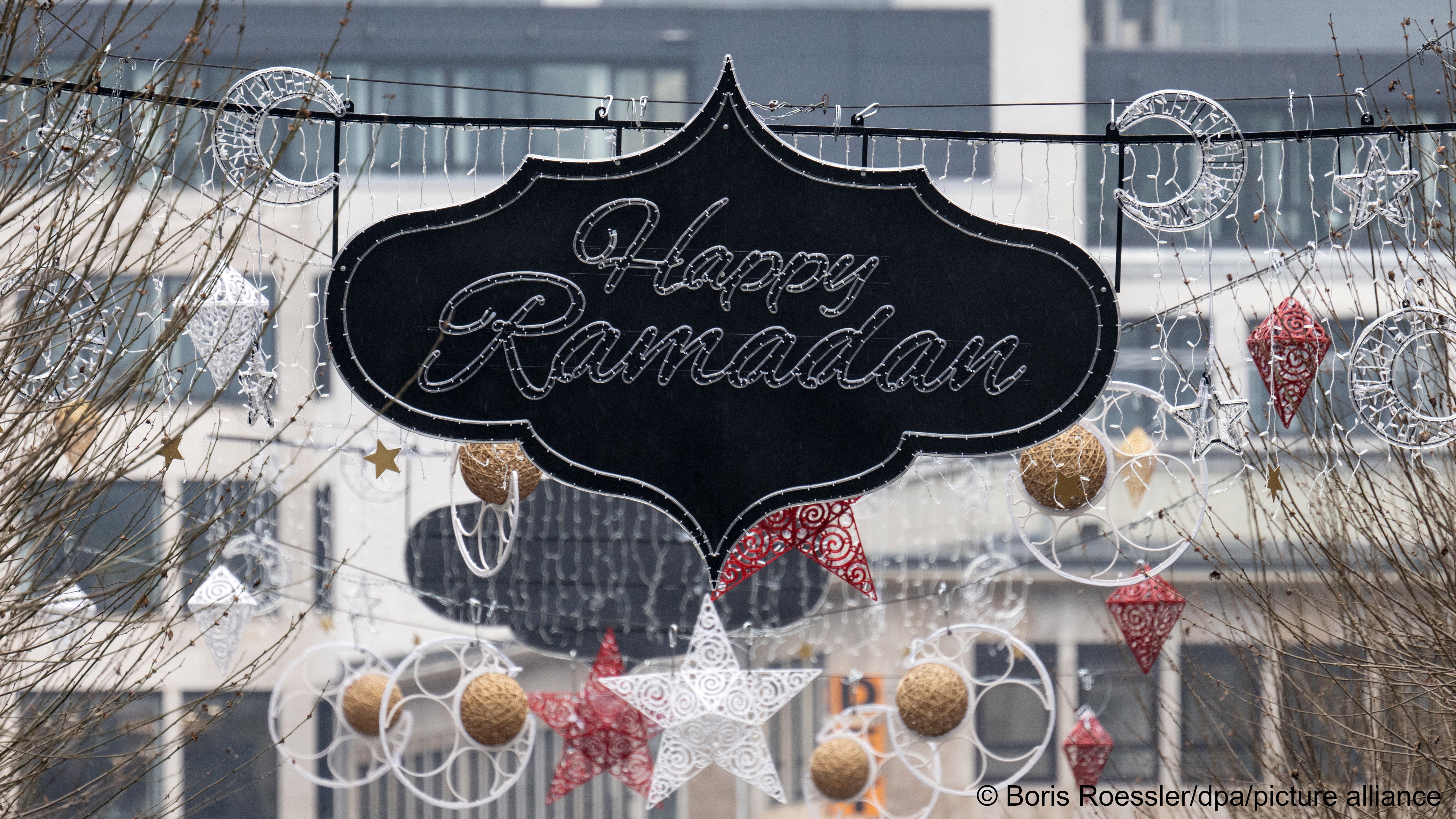 A black sign that reads 'Happy Ramadan' in lights is seen suspended over a street in Frankfurt, Germany, 5 March 2024., Behind it are sparkly crescents, stars, orbs and decorative circles in white, silver, red and gold