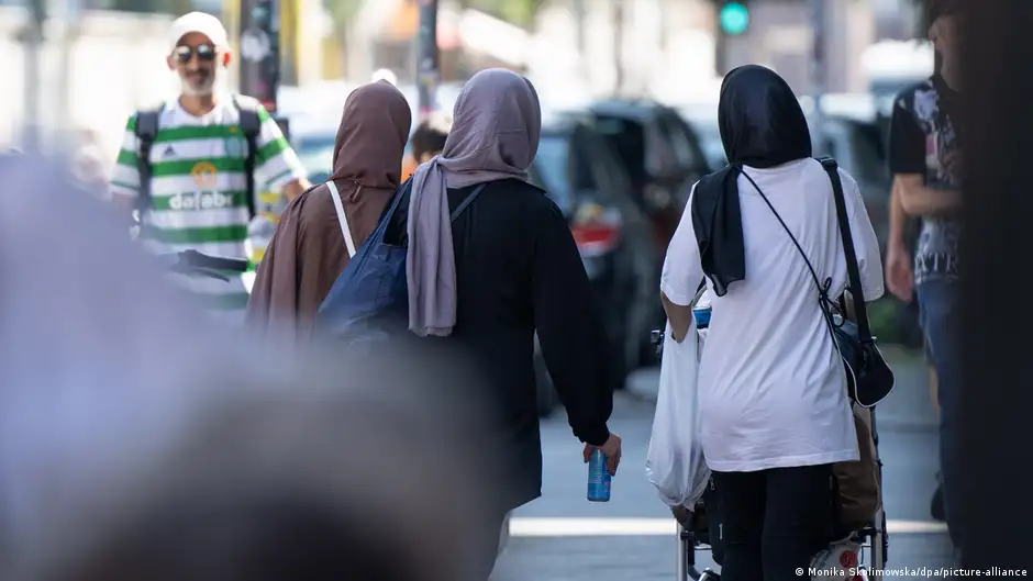 Three woman wearing headscarves are seen from behind walking along a street