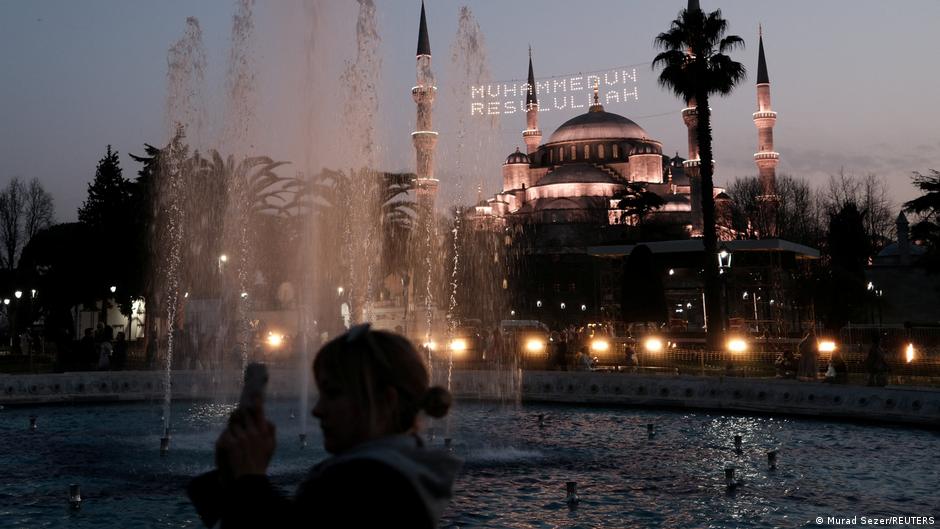 Hell erleuchtet und mit einem religiösen Schriftzug versehen steht die Blaue Moschee in Istanbul in der Dämmerung