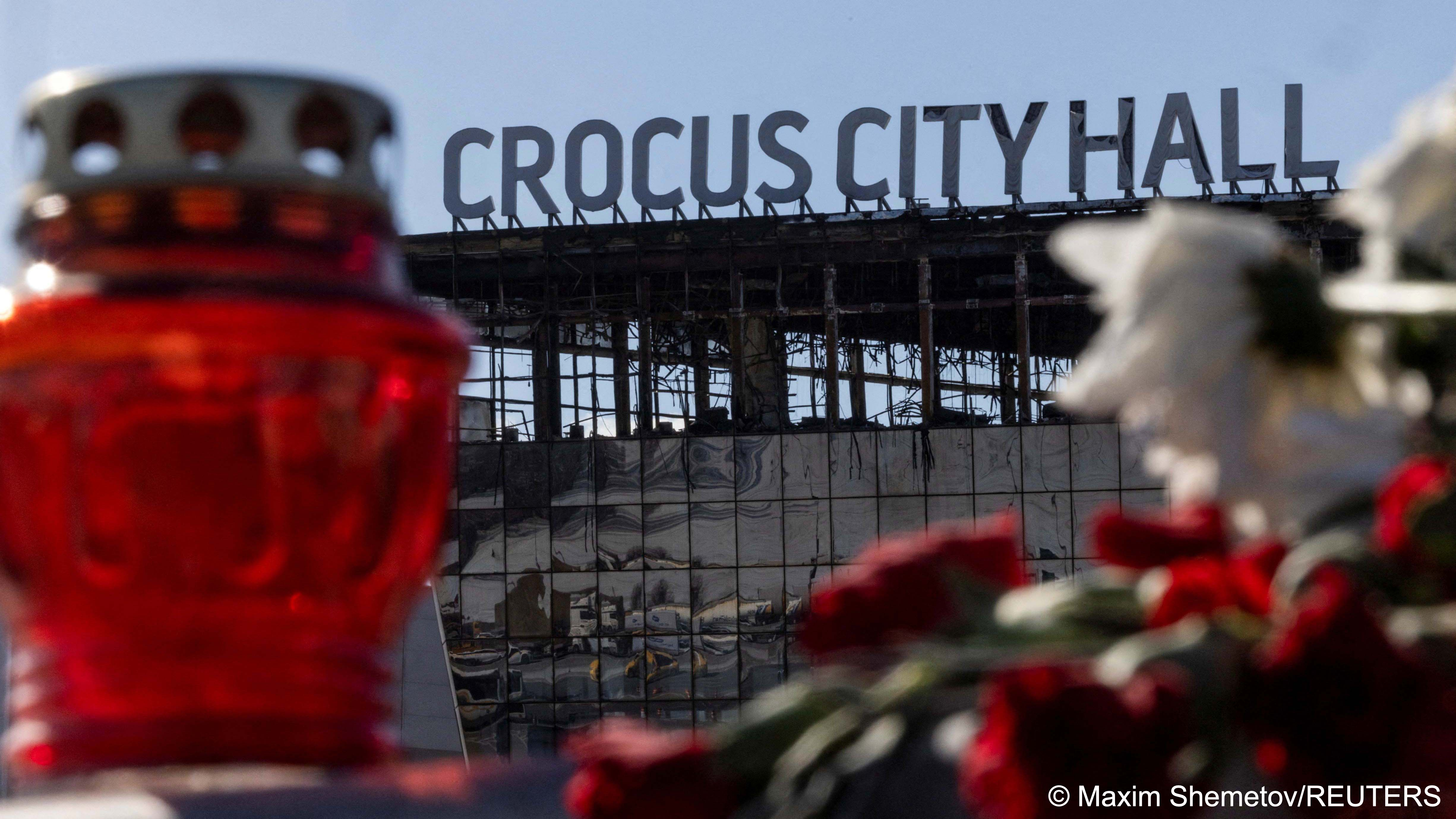 The burnt-out shell of Crocus City Hall following the deadly attack on the concert venue is seen behind a candle and some red and white flowers, Moscow Region, Russia, 27 March 2024