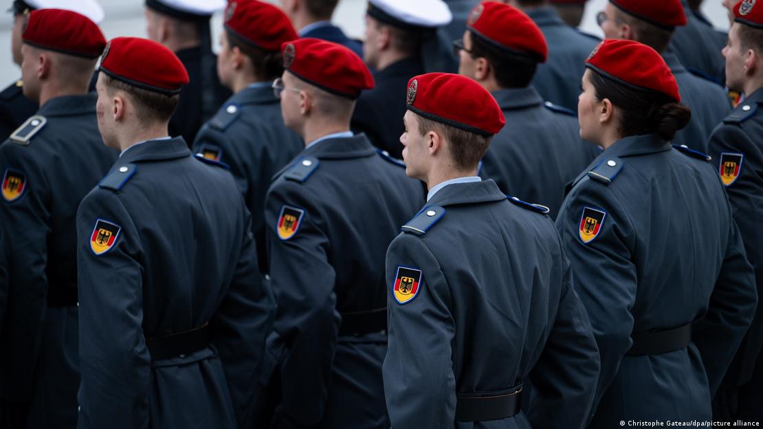 Several rows of German army recruits wearing ceremonial service uniforms stand in formation with their backs to the camera, November 2023