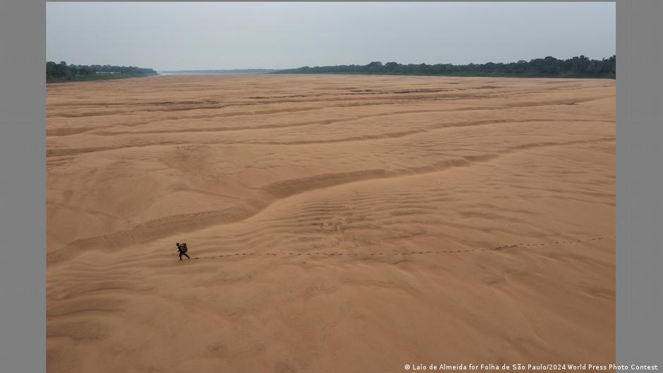 A fisherman crosses a sandy expanse that is a dried up section of the Amazon River.