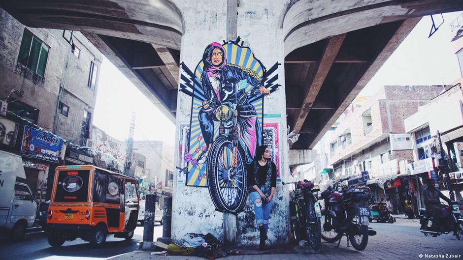 Fashion model Eman Suleman poses in front of graffiti done by Shehzil Malik under a bridge in Lahore, Pakistan
