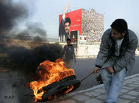 A Hezbollah supporter moves a burned tire in front a huge poster of Hezbollah leader Sheik Hassan Nasrallah (photo: AP)