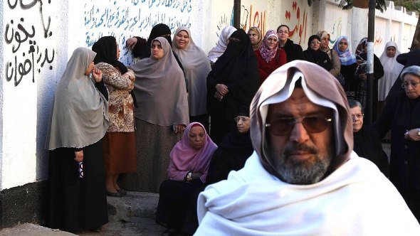 نساء يقفن في طابور بجانب رسوم جدارية مناوئة للحكومة في مصر. رويترز