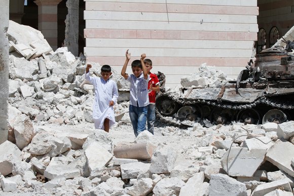 Kinder spielen auf einem Trümmerfeld vor einer Moschee und einem zerstörten Panzer in Azaz; Foto: Joshua Archer